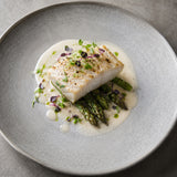 Plated dish of white fish with asparagus and a creamy sauce made with verjus on a grey plate.