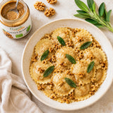 Plate of ravioli pasta with organic walnut butter, chopped raw walnuts and fresh sage leaves on a light background.