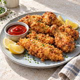 A plate of crispy fried chicken made with a white rice flour batter, served with ketchup and lemon wedges.