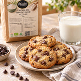 A plate of chocolate chip cookies on a tabletop beside a glass of milk, with a bag of Monika's Kitchen Organic White Rice Flour.