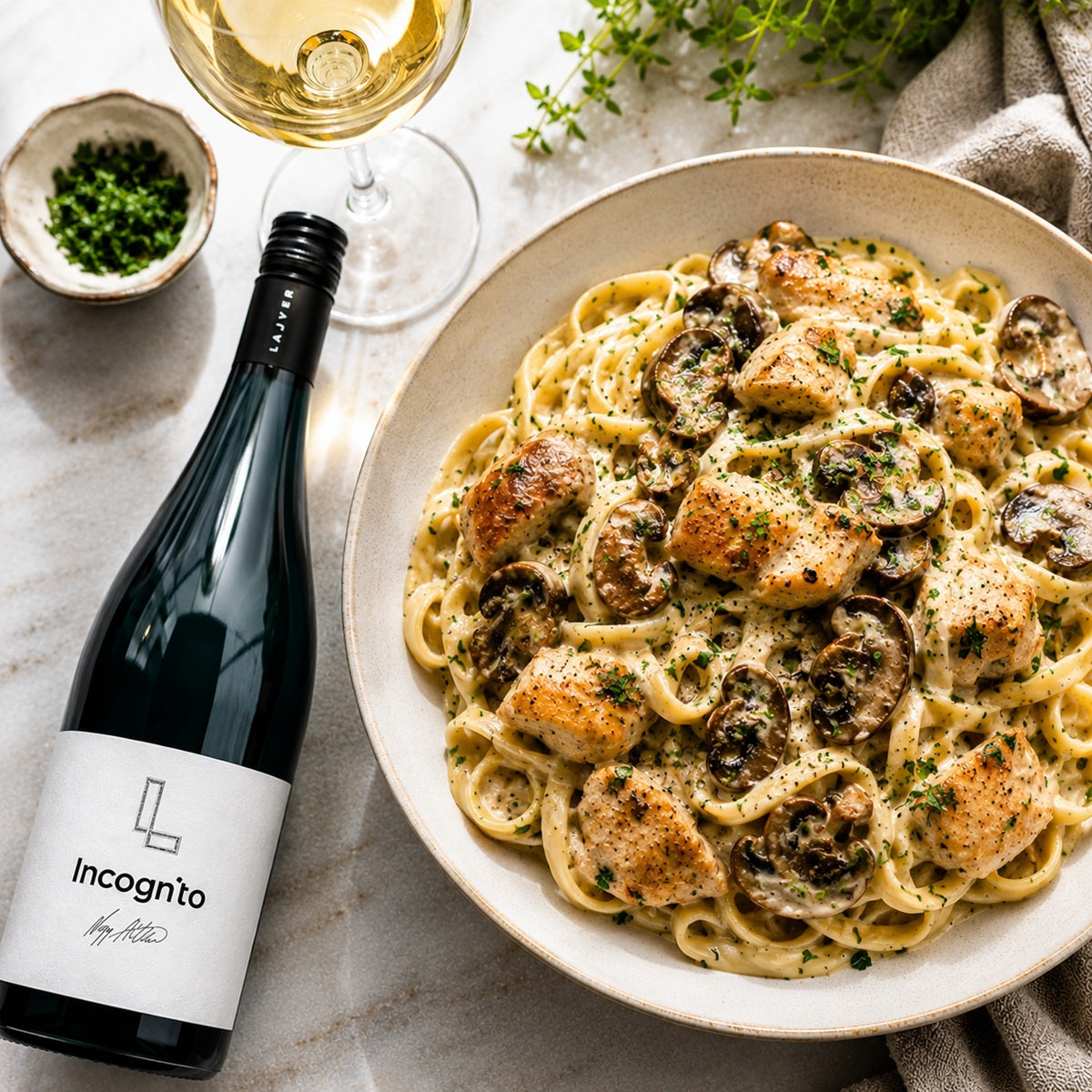 Plate of creamy pasta with chicken and mushrooms paired with a bottle of white wine on a marble surface.