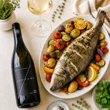 A bottle of Kreinbacer Juhfark white wine with plate of grilled fish served on a bed of vegetables.