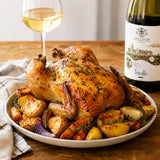 Roasted chicken with vegetables on a plate next to a glass of white wine and a bottle of Tricollis wine.