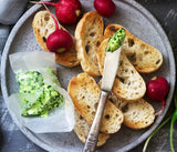 Platter of bread slices with wild garlic butter and radishes on a grey surface.