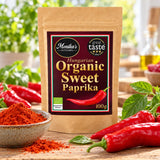 Monika's Kitchen Organic Sweet Paprika pouch beside red peppers and a bowl of vivid paprika powder.