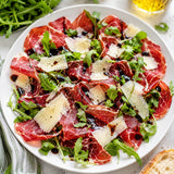 Plate of ham carpaccio with mangalitza ham slices, Parmesan shavings, rocket and balsamic vinegar.